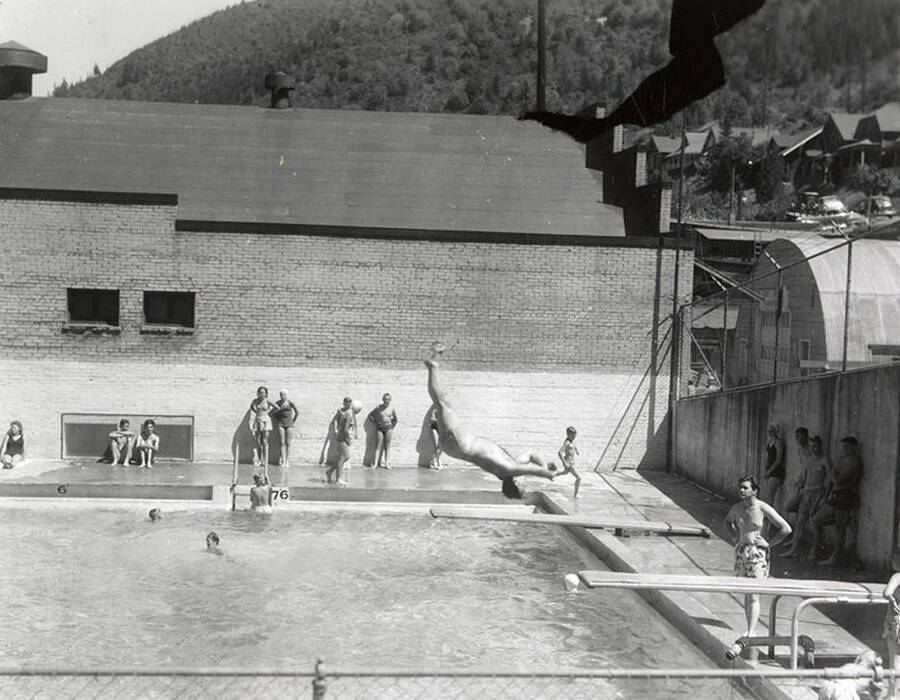 Jack Foster diving in the swimming pool in Wallace, Idaho. Others stand around the pool, watching.