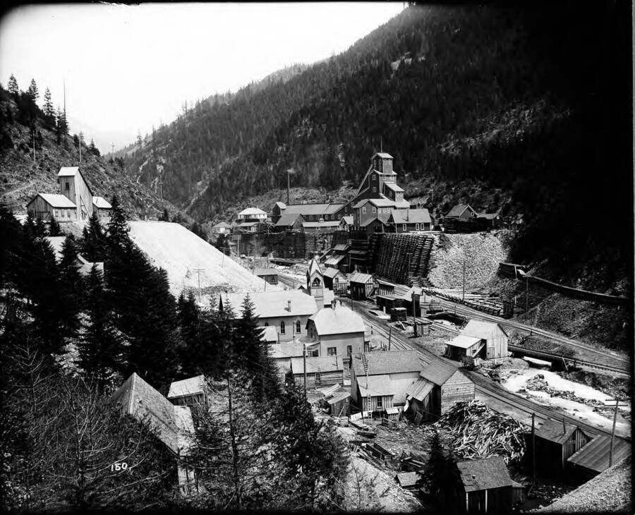 Hecla Mine in Burke, Idaho. This view includes a church and several other buildings along the railroad tracks.