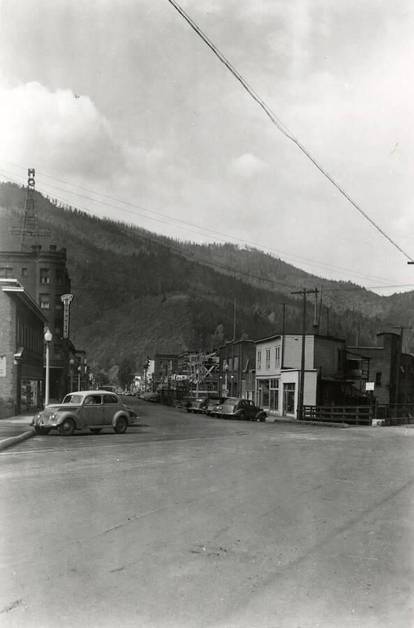 View looking down Cedar Street in Wallace, Idaho. Stores, with cars parked out front, line the street.