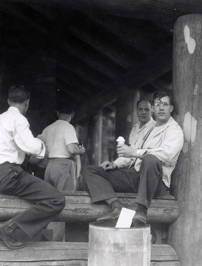 A few men sitting on a log and eating ice cream during Wallace Jaycee's picnic in Pottsville, Idaho.