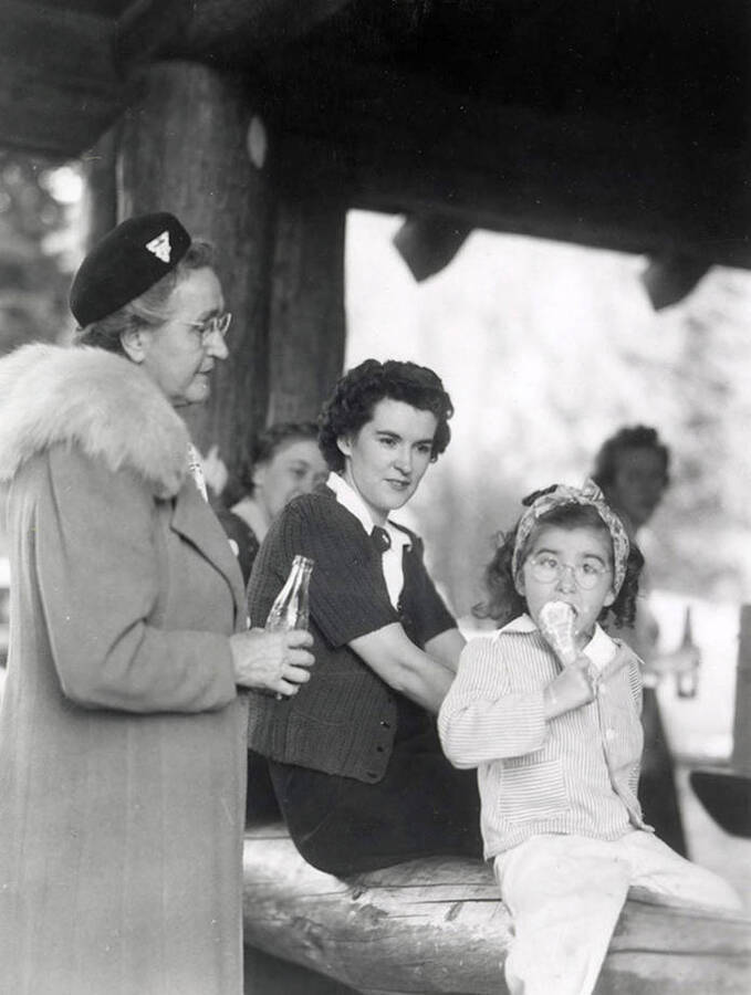 A girl eating ice cream, while some other women sit around, during Wallace Jaycee's picnic in Pottsville, Idaho.