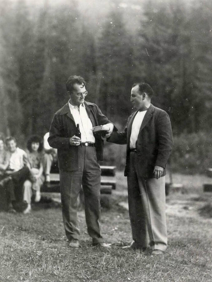 Two men standing together during Wallace Jaycee's picnic in Pottsville, Idaho. One man is giving the other a small package.