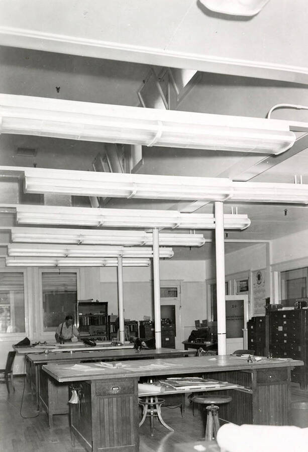 Interior view of the Day Mines Engineering office in Wallace, Idaho. A man can be seen working at one of the desks.