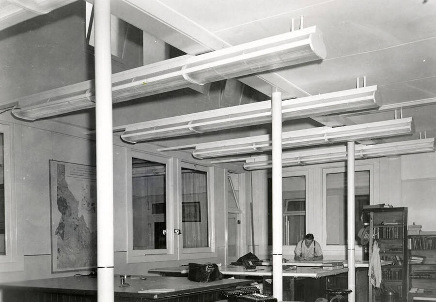 Interior view of the Day Mines Engineering office in Wallace, Idaho. A man can be seen working at one of the desks.