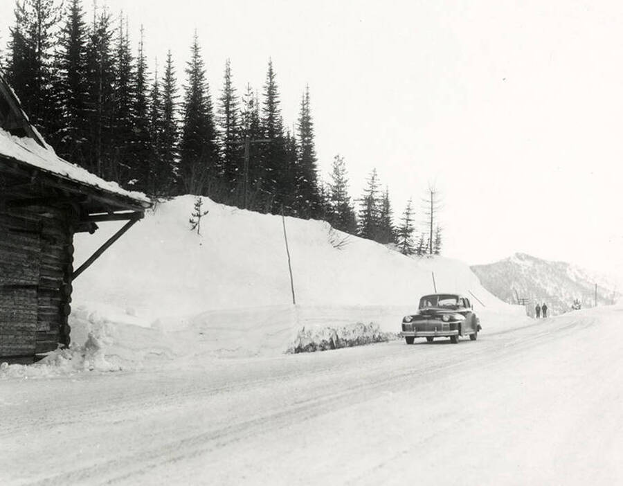 View of Lookout Pass covered in snow. A car is parked on the side of the road and two men are walking in the distance. Taken for Farmers Insurance Company.