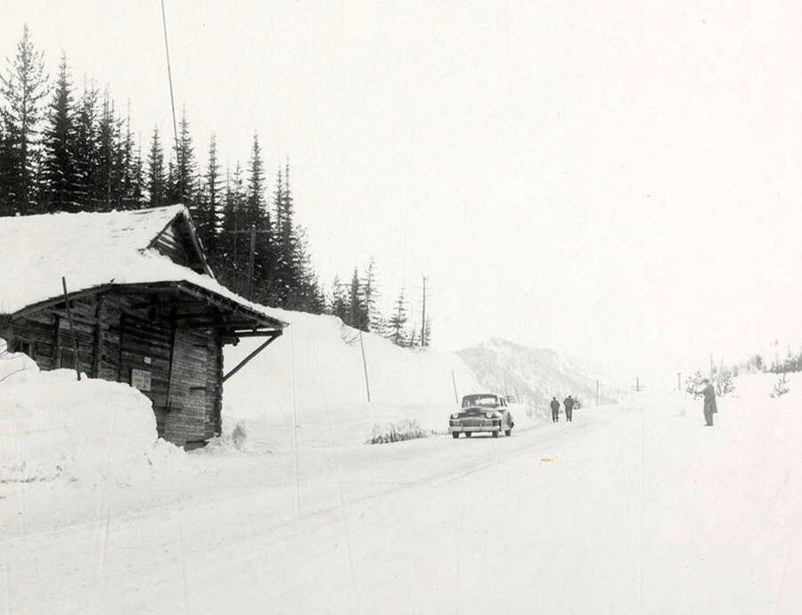 View of Lookout Pass covered in snow. A car is parked on the side of the road and a few men are walking in the distance. Taken for Farmers Insurance Company.