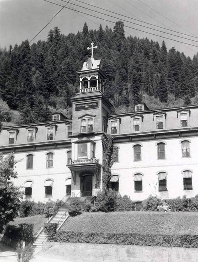 Exterior view of Providence Hospital in Wallace, Idaho. A hill covered in trees can be seen behind the hospital.
