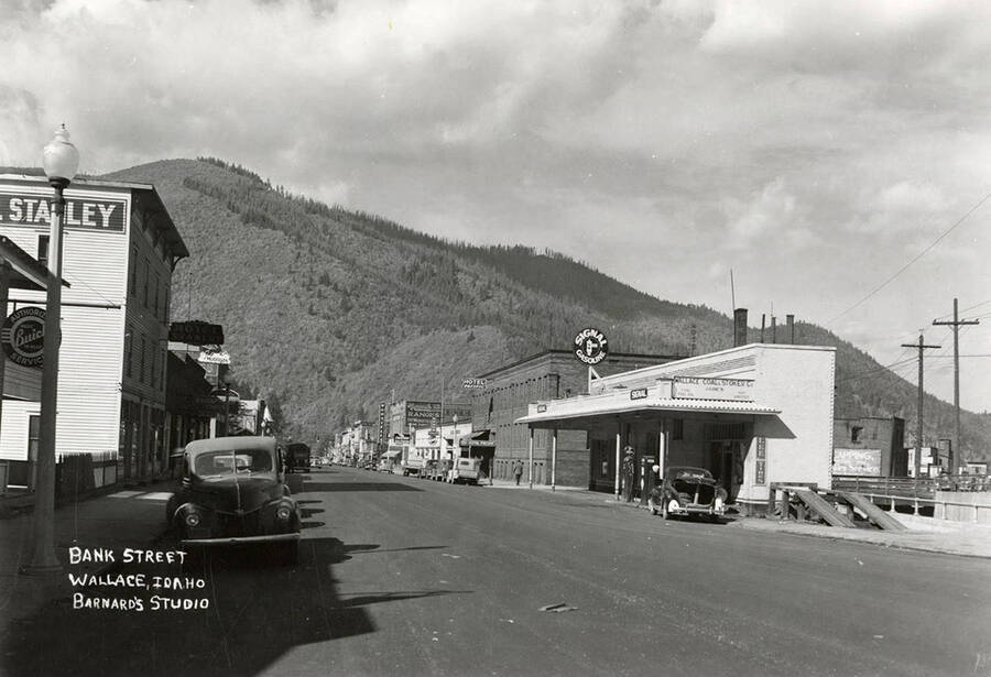 View looking down Bank Street in Wallace, Idaho. Stores, with cars parked out front, line the street.