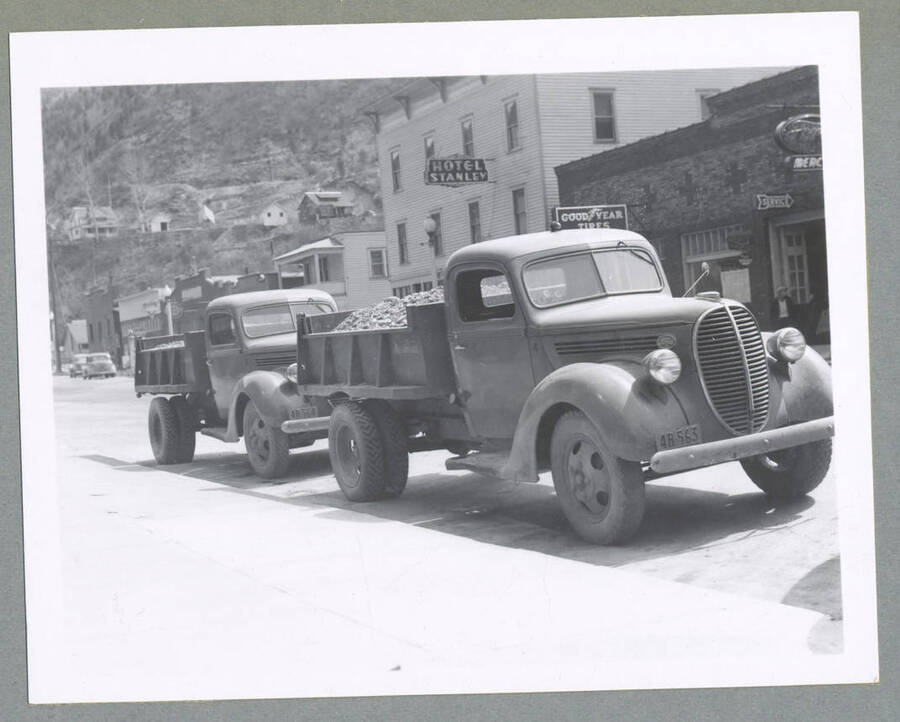 Trucks with first shipment of ore from Silver Cable Mine, with the Stanley Hotel and Good Year Tires store in the background.