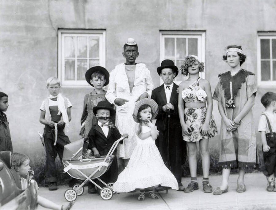Children in costumes with homemade props during the 49'er Parade in Mullan, Idaho. One child is wearing blackface makeup.
