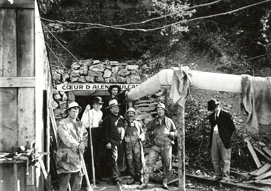 A group of men standing at the entrance to the Coeur d'Alene Vulcan Mine in Wallace, Idaho. The Vulcan Mine is the secondary name for the Galena Mine