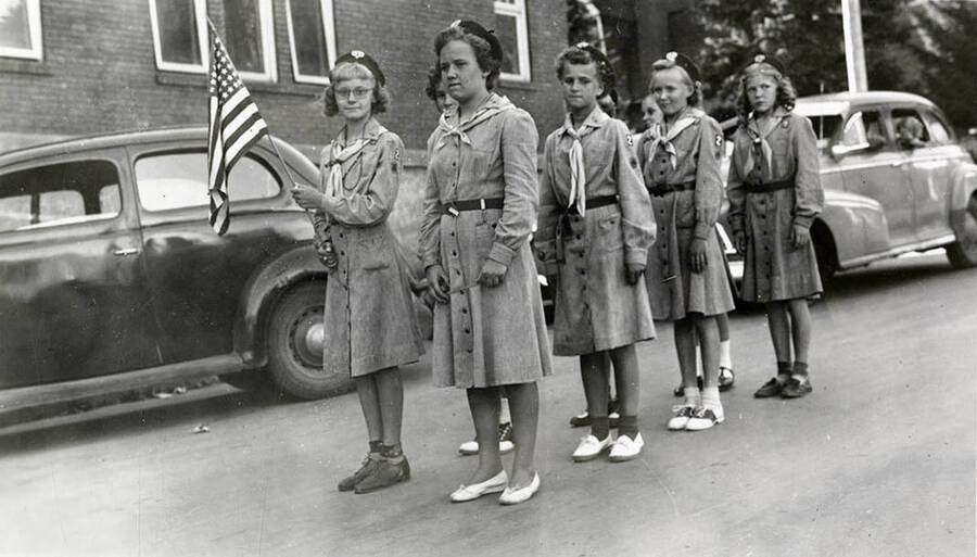 A group of Girl Scouts standing in line behind the American flag during the 49'er Parade in Mullan, Idaho.