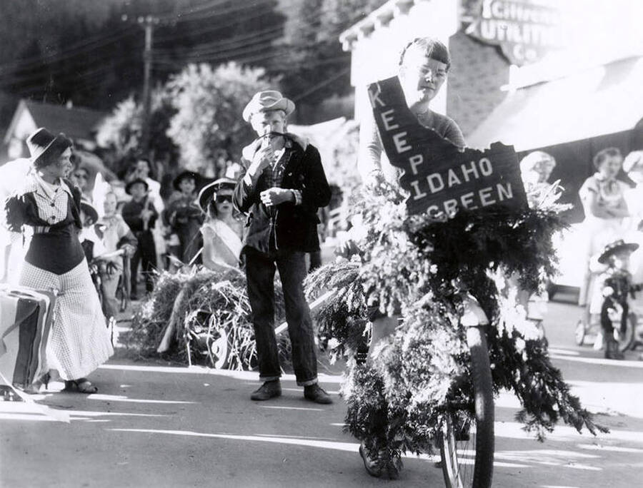 A woman riding a bike decorated with greenery and an Idaho-shaped sign that reads, "KEEP IDAHO GREEN" during the 49'er Parade in Mullan, Idaho.