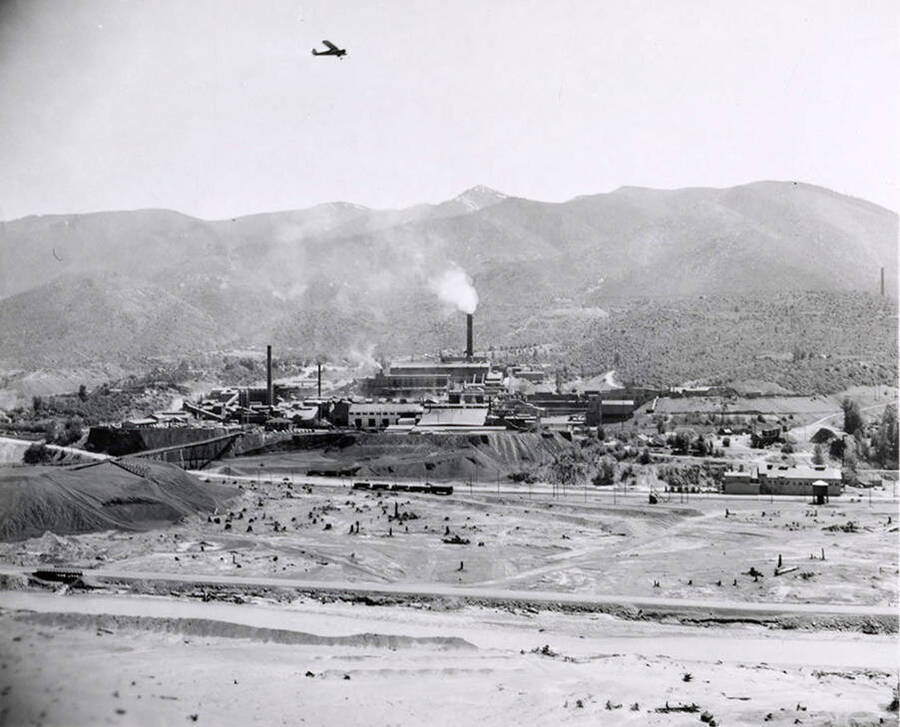 A hillside view of the Bunker Hill and Sullivan Smelter with an airplane flying overhead in Bradley, Idaho.