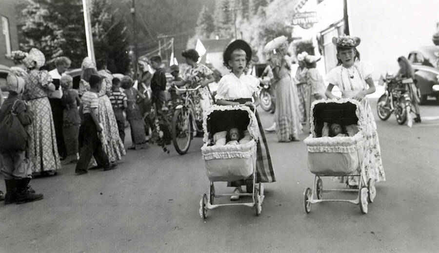 Two young girls pushing baby dolls in strollers during the 49'er Parade in Mullan, Idaho.