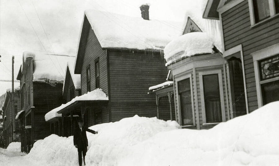Residential houses covered in snow in Wallace, Idaho. A man can be seen standing next to a snow bank.