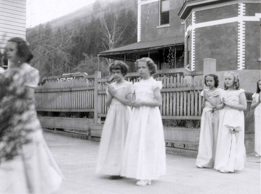 Girls walking in pairs along the sidewalk outside of Our Lady of Lourdes Academy during the Blessed Virgin Procession in Wallace, Idaho.