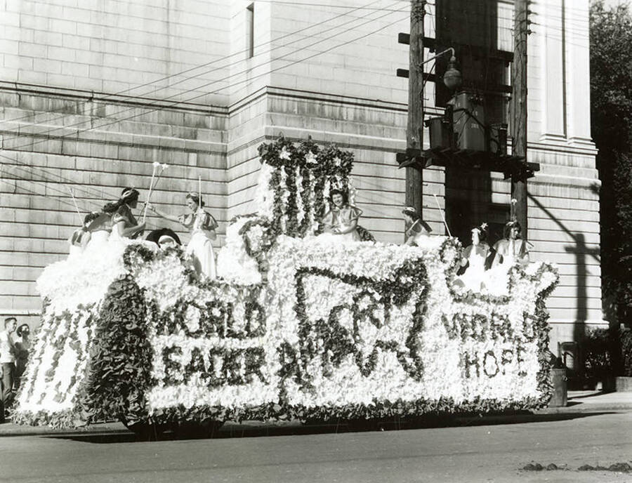Women wearing tiaras and holding wands riding atop a large float with signage that reads, "1951 / World Leader / America / World Hope" during the Elks Parade in Wallace, Idaho.