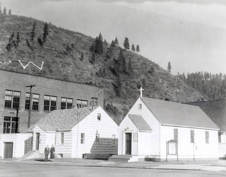 Rev. Martin A. Russert and his wife standing on the sidewalk in front of Bethany Lutheran Church and parsonage in Wallace, Idaho.