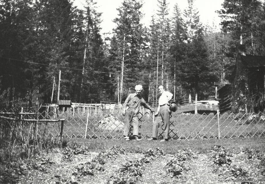 Two men standing against a wooden fence at Tobs cabin near Wallace, Idaho.