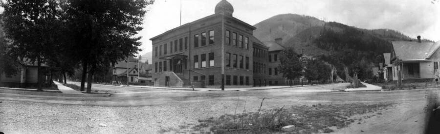View of street corner with Wallace High School and houses. Panoramic photograph of Wallace, Idaho.