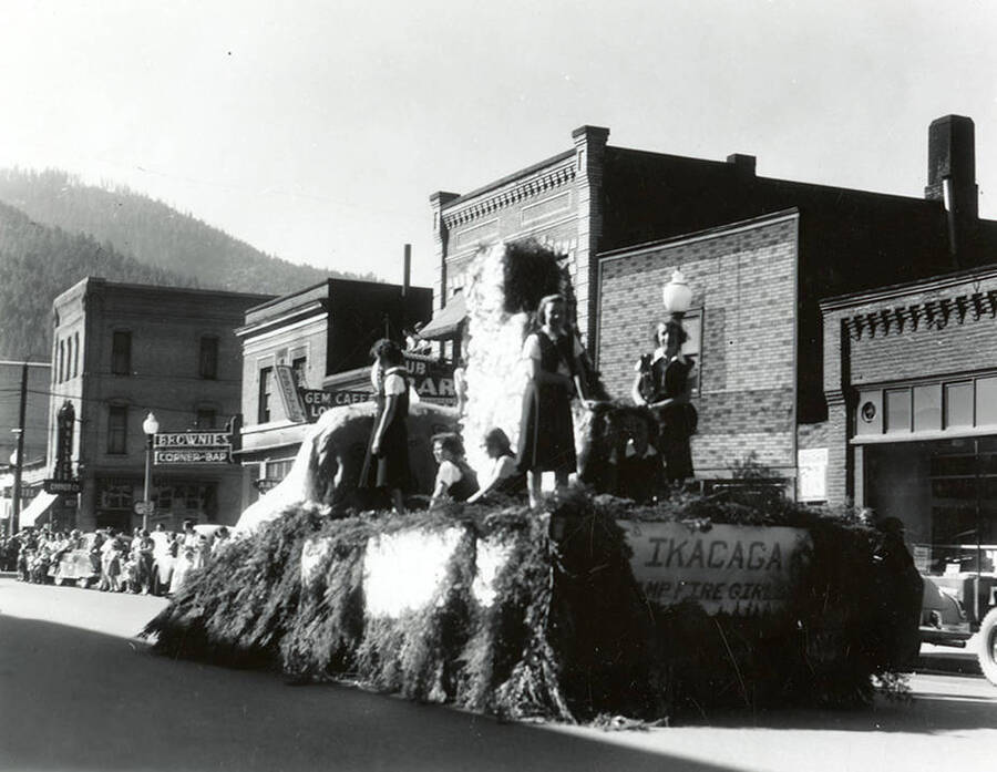 A group of girls standing on a float during the Elks Parade in Wallace, Idaho. A sign on the back of the float reads: "IKACAGA / Camp Fire Girls."