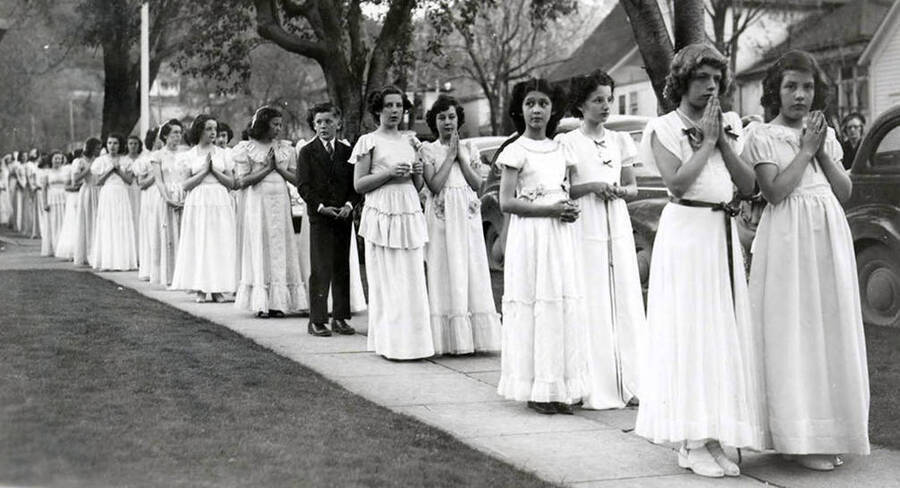 Girls and one boy lined up on the sidewalk outside of Our Lady of Lourdes Academy during the Blessed Virgin Procession in Wallace, Idaho.