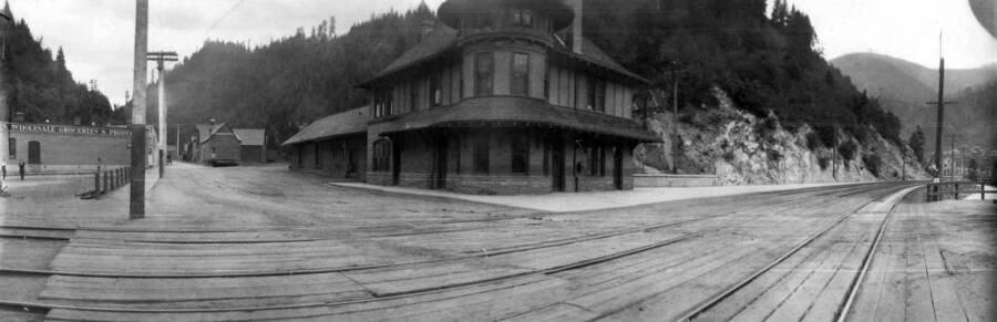 View of railroad tracks with town buildings in the background. Panoramic photograph of Wallace, Idaho.