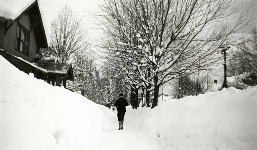 A person walking down the sidewalk of a snow covered Pine Street in Wallace, Idaho.