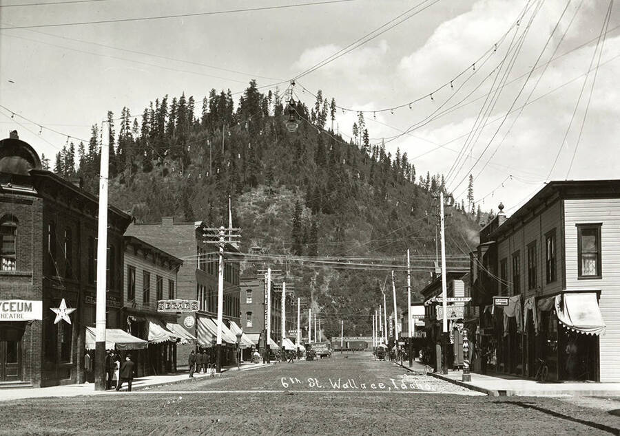 View looking down Sixth Street in Wallace, Idaho. People can be seen standing on the sidewalk, in front of the buildings.