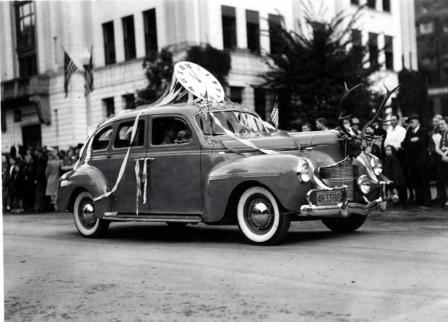 A small car covered in streamers with a fake clock on the roof. On the front, antlers are mounted.