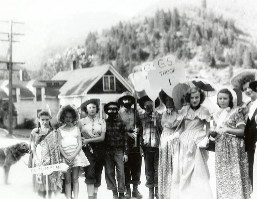 A group of people dressed for the Elks Parade in Wallace, Idaho. Some are holding signs that say "G.S. Troop 1."