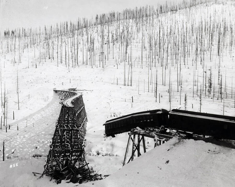 Distant view of the  ruined "S" bridge, with a passenger car hanging precariously from the tracks. The trestle was wiped out by a massive snow slide in 1903.