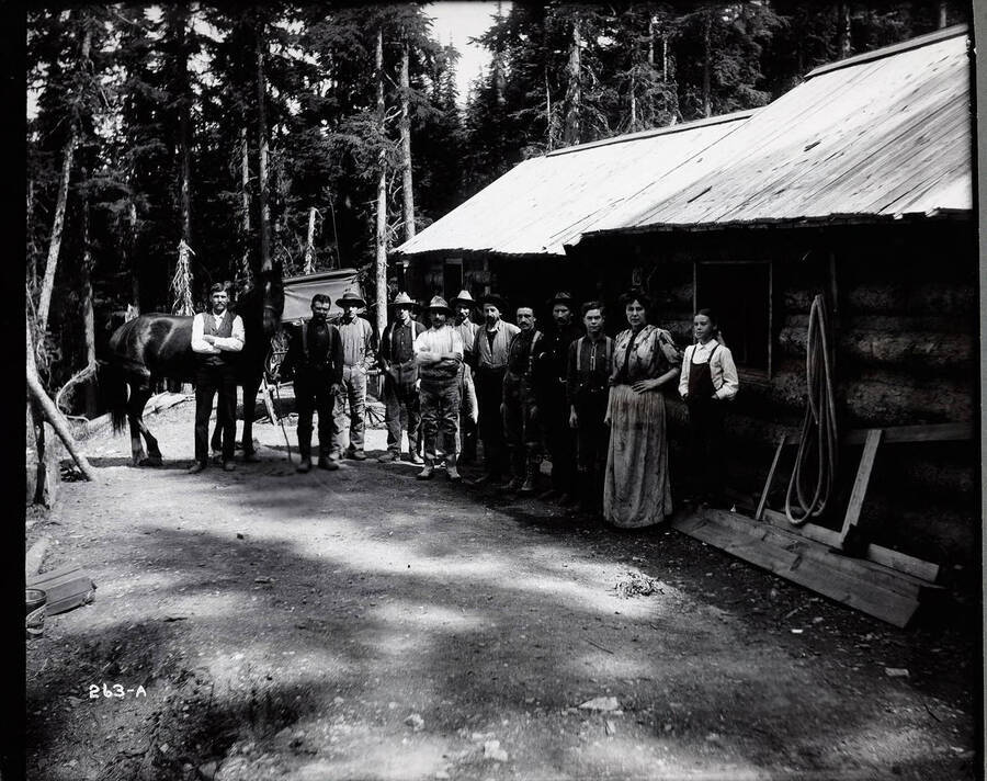 This photo shows a group of twelve people and one horse, standing in front of a log building on the Laclede Mine property.