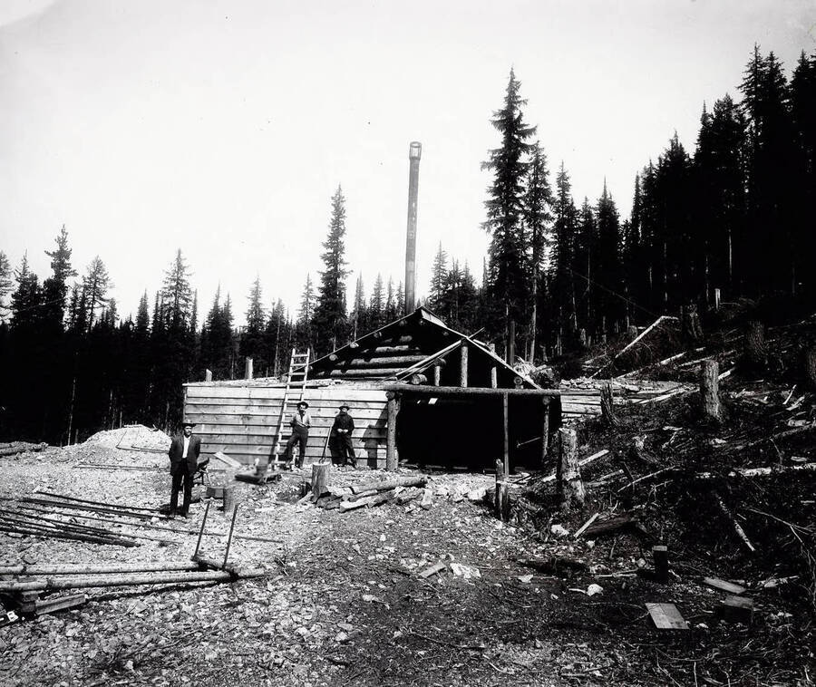 Image shows three men standing by a ladder in front of a log/wooden building on the Laclede Mine property. According to University of Idaho Manuscript Group 242 description, the Laclede Mine was explored, but found to contain limited commercial ore.