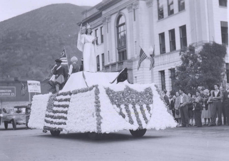 A woman dressed as Lady Liberty standing atop a float decorated with the American flag.
