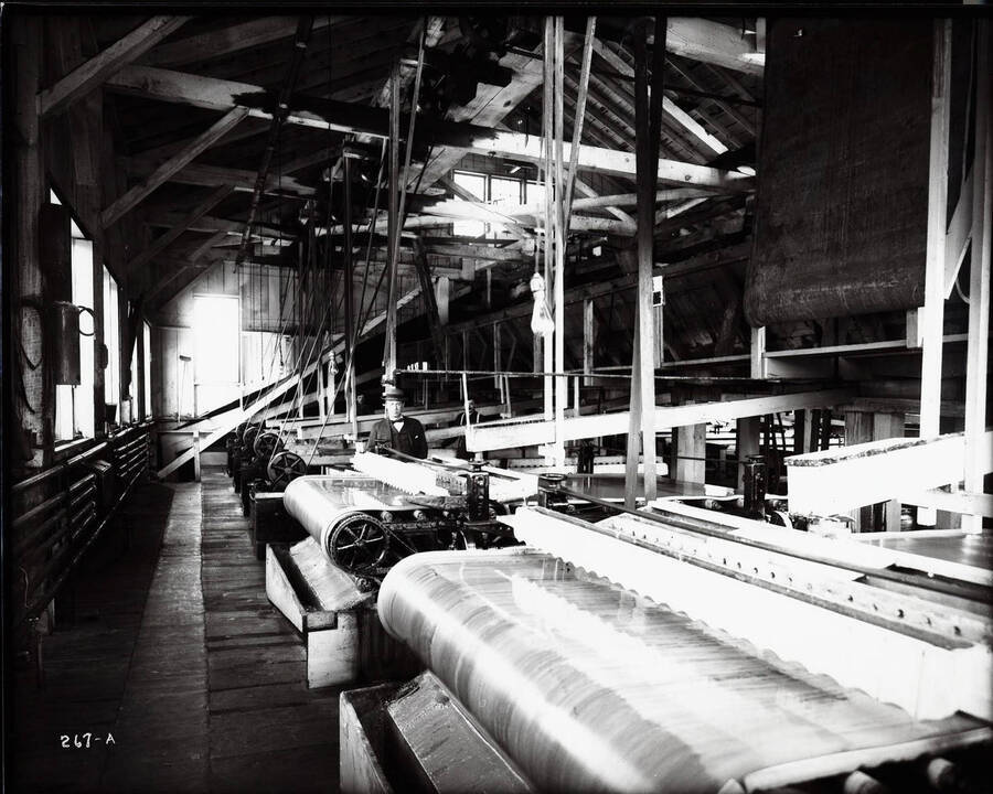 Interior view of the Sweeney Mill, located near Smelterville, Idaho. Three workers are surrounded by large pieces of machinery.