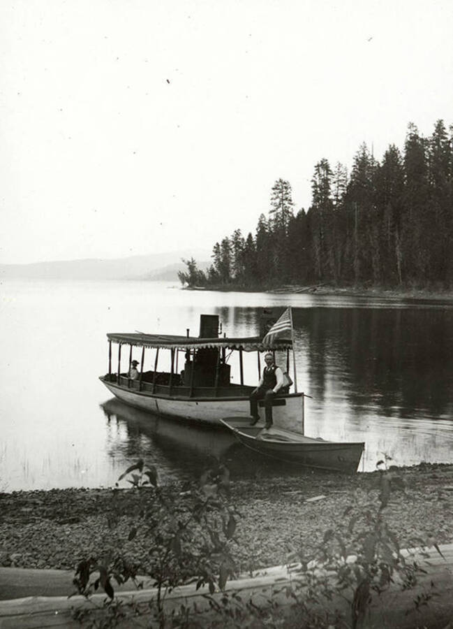 Steam launch on Lake Coeur d'Alene. A man sits on a boat in the lake.