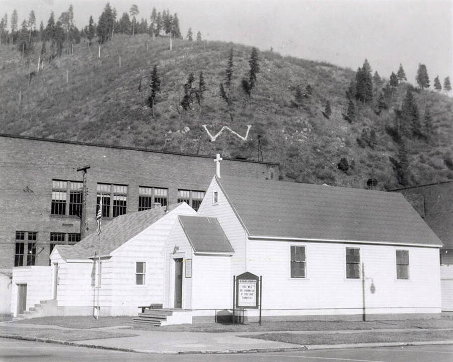 Rev. Martin A. Russert and his wife standing on the sidewalk in front of Bethany Lutheran Church and parsonage in Wallace, Idaho.