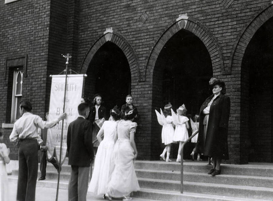 Children, some wearing angel wings, walking in pairs into the Our Lady of Lourdes Academy building during the Blessed Virgin Procession in Wallace, Idaho.