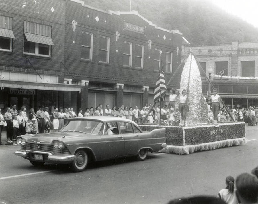 Floats being driven in the Jubilee parade in Wallace, Idaho. Women are sitting and standing on the float.