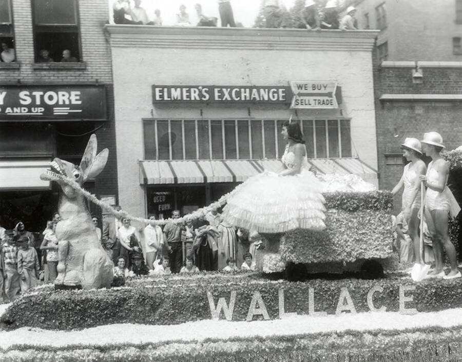 Floats being driven in the Jubilee parade in Wallace, Idaho. Women are sitting and standing on the float.