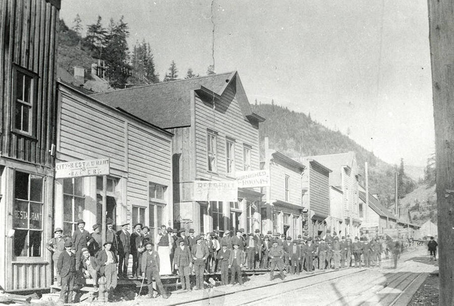 View of a street in Burke, Idaho. Residents can be seen standing in front of stores on the street.