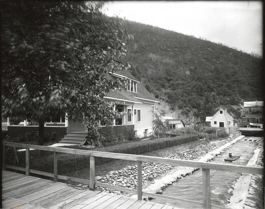 Exterior view of J.E. Gyde House in Wallace, Idaho. You can see a person in a small boat floating on the river in the photograph.