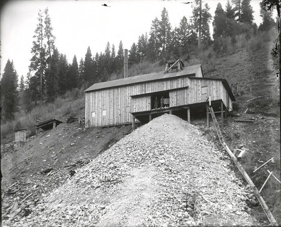 Exterior of the Evolution Mine in Osburn, Idaho. There is a large rock pile and shute beneath the open door.