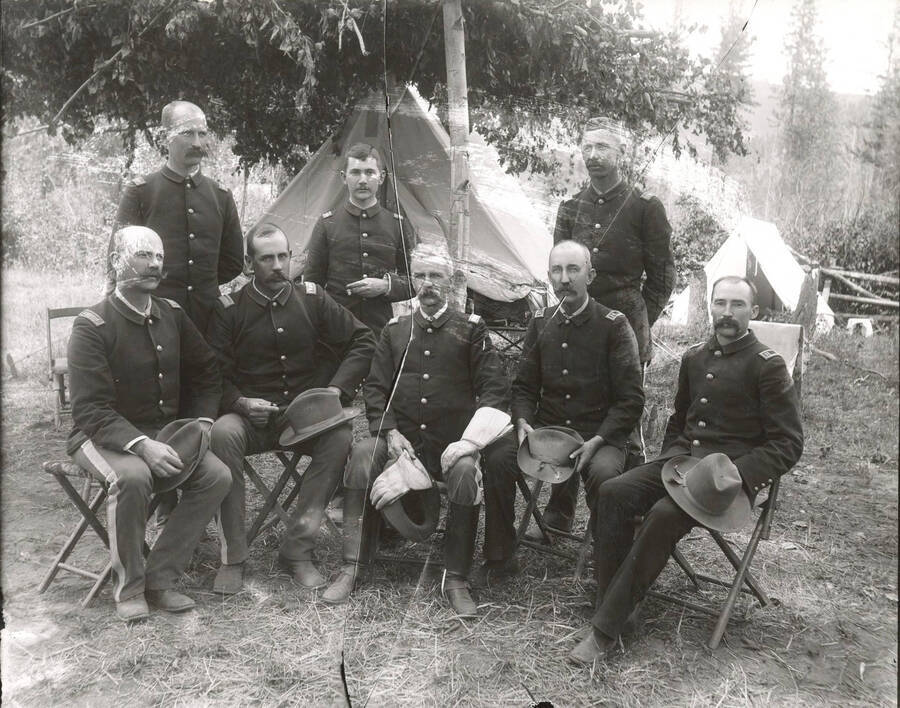 Five soldiers seated in folding chairs with three others standing. Three large cracks and some scuffing on the negative occurred prior to this photograph being printed.