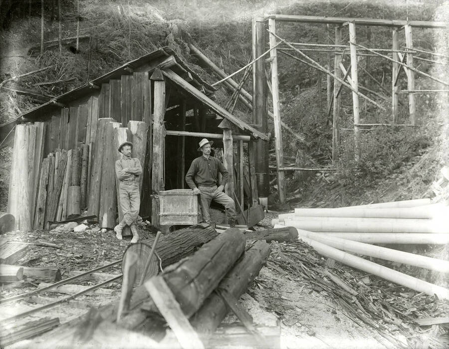 View of an unidentified mine located above Wardner, Idaho. Two men can be seen standing in front of a building on the mine.