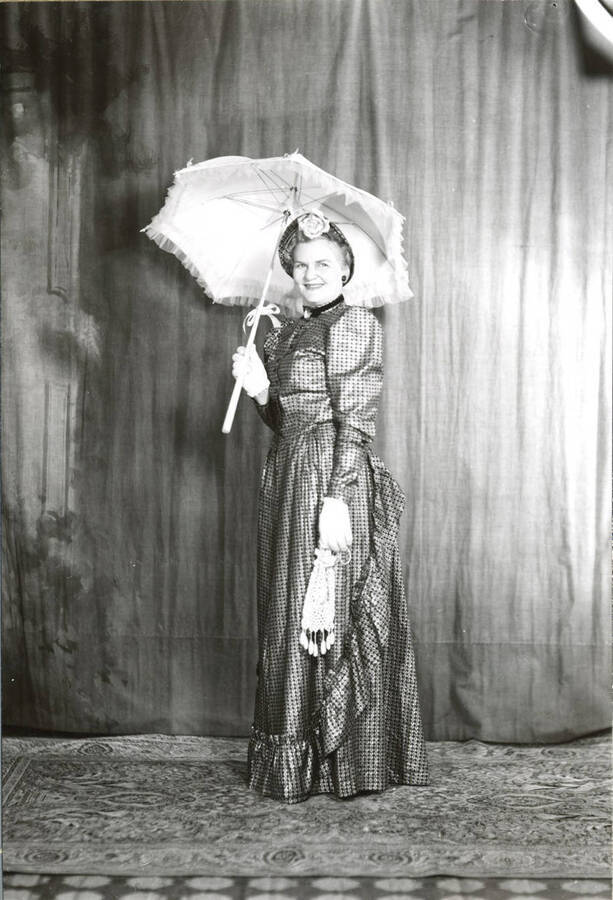 Formal portrait of a lady in a bustled gown holding an parasol and knit hand bag.