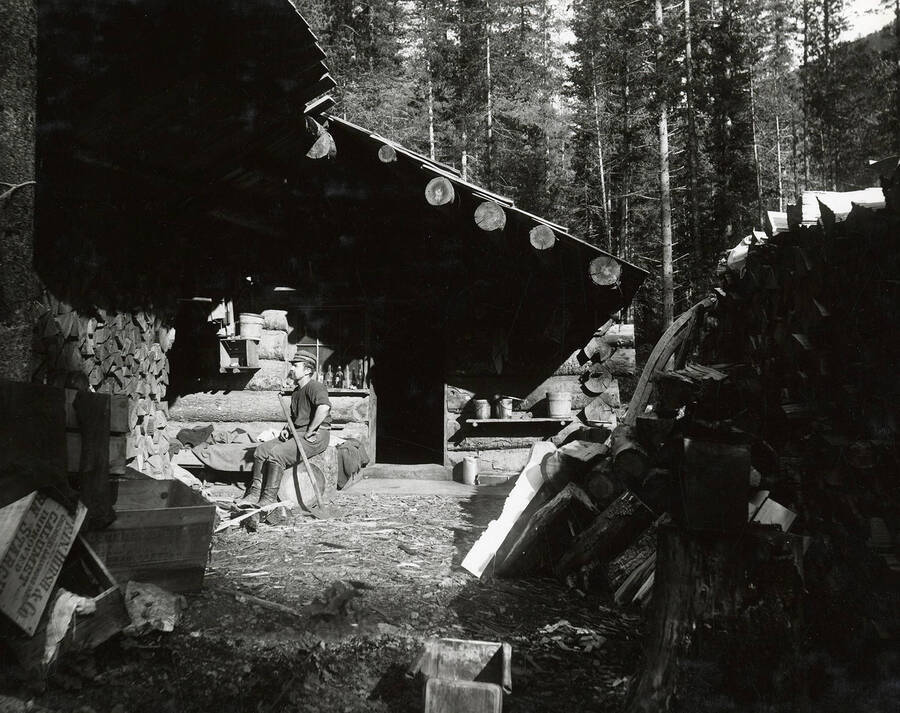 The Sny Bar Cabin at East Eagle Creek. A man can be seen sitting outside of a cabin with mining equipment around him