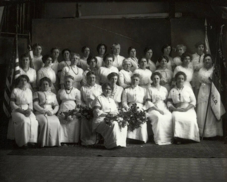 Group photo of thirty women involved in the Women's Benefit Association of the Maccabees in Wallace, Idaho. Pictured are the United States flag and the Maccabees flag.